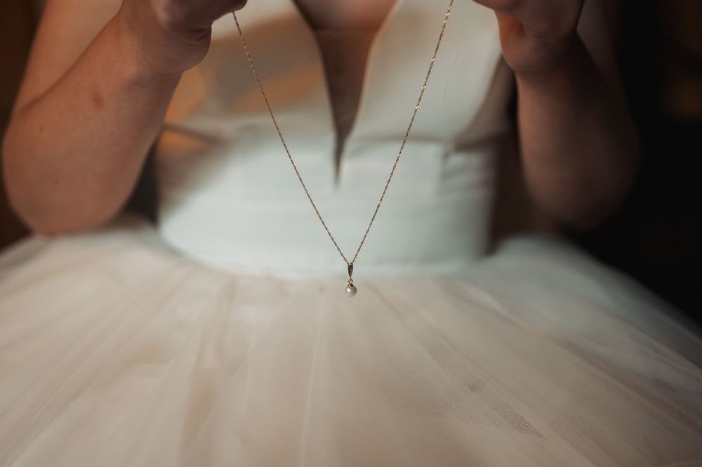 Close-up detail of a delicate necklace against a white wedding dress bodice and tulle skirt.