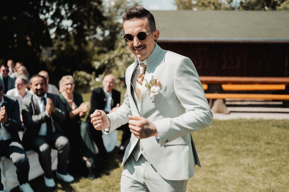 Wedding guests dance and celebrate outdoors on a sunny day at a garden reception.