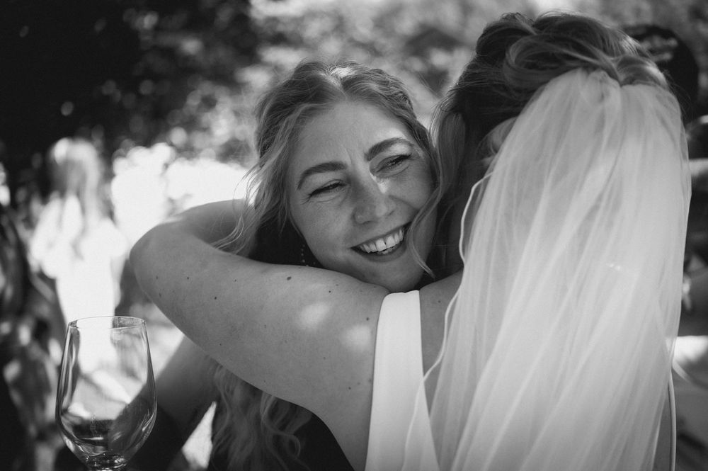 A candid black and white photograph captures a joyful embrace at an outdoor wedding celebration.