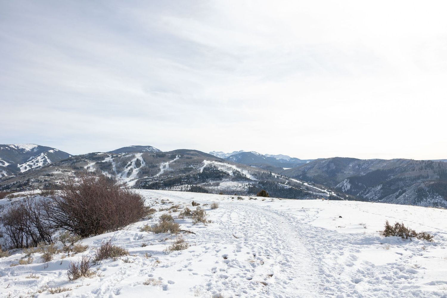 A snowy hiking trail winds through brown sagebrush and desert hills on a winter day in the wilderness.