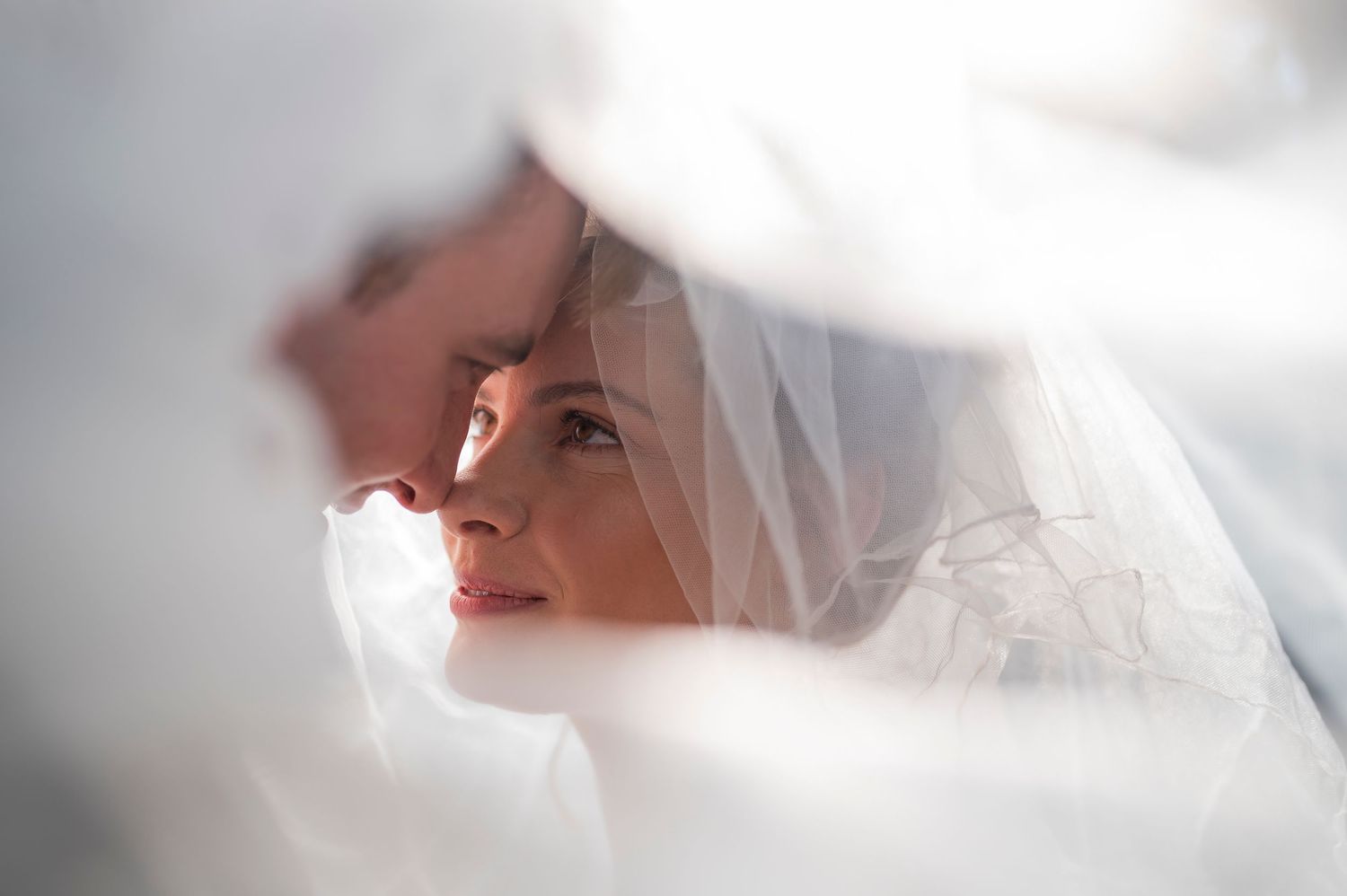 A bride wearing a delicate white veil is photographed in soft ethereal lighting creating a romantic bridal portrait.