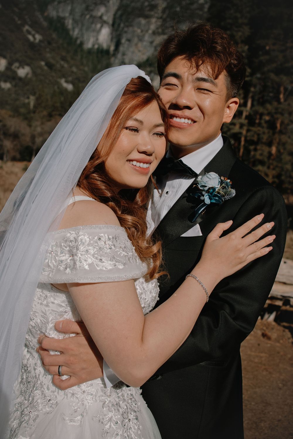 A joyful couple embraces outdoors during their wedding photoshoot wearing traditional formal attire.