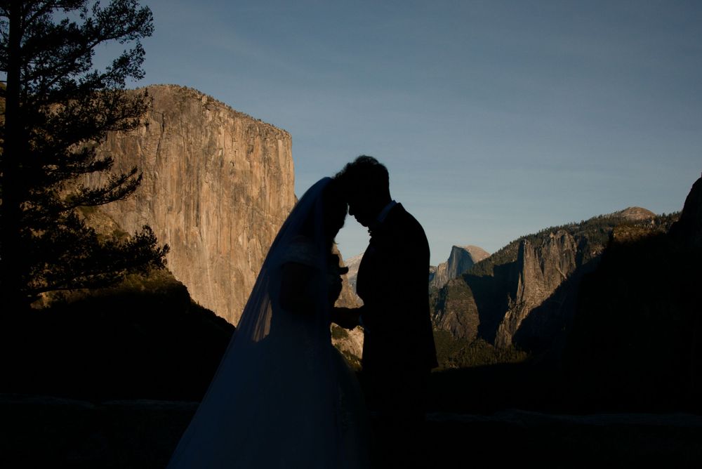 A silhouetted couple embraces while standing against the backdrop of Yosemite Valley at sunset after their chapel elopement.