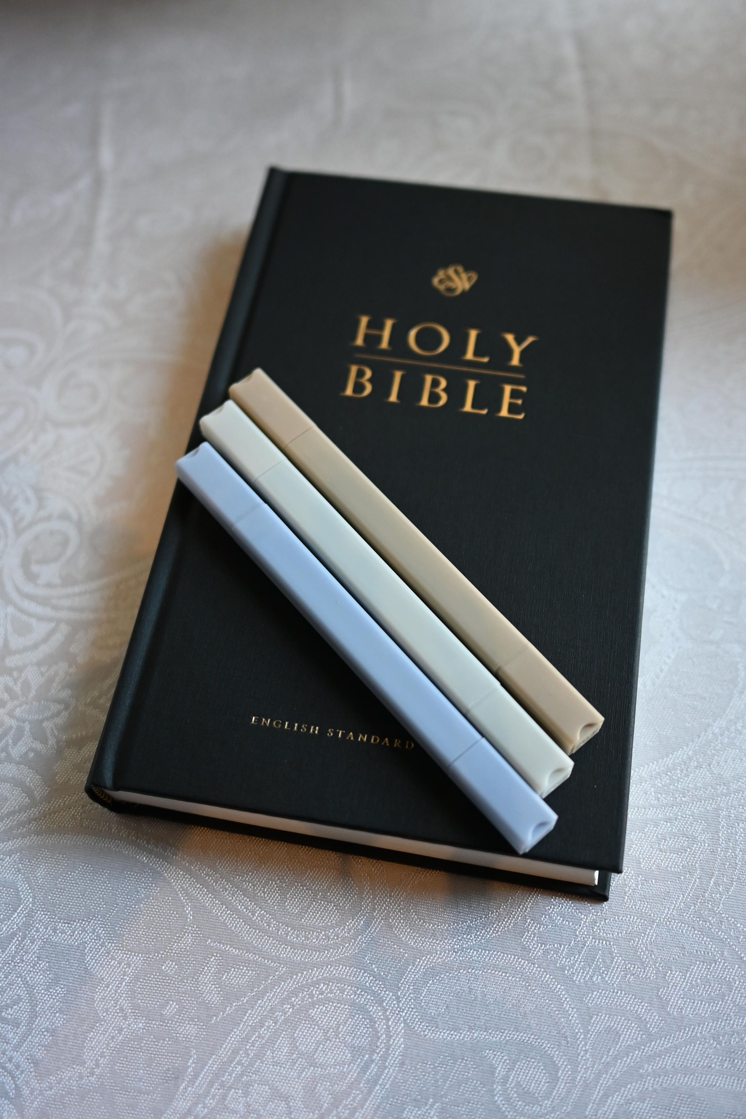 A black leather Holy Bible with gold lettering lies on a textured white surface with a cigarette placed on top.