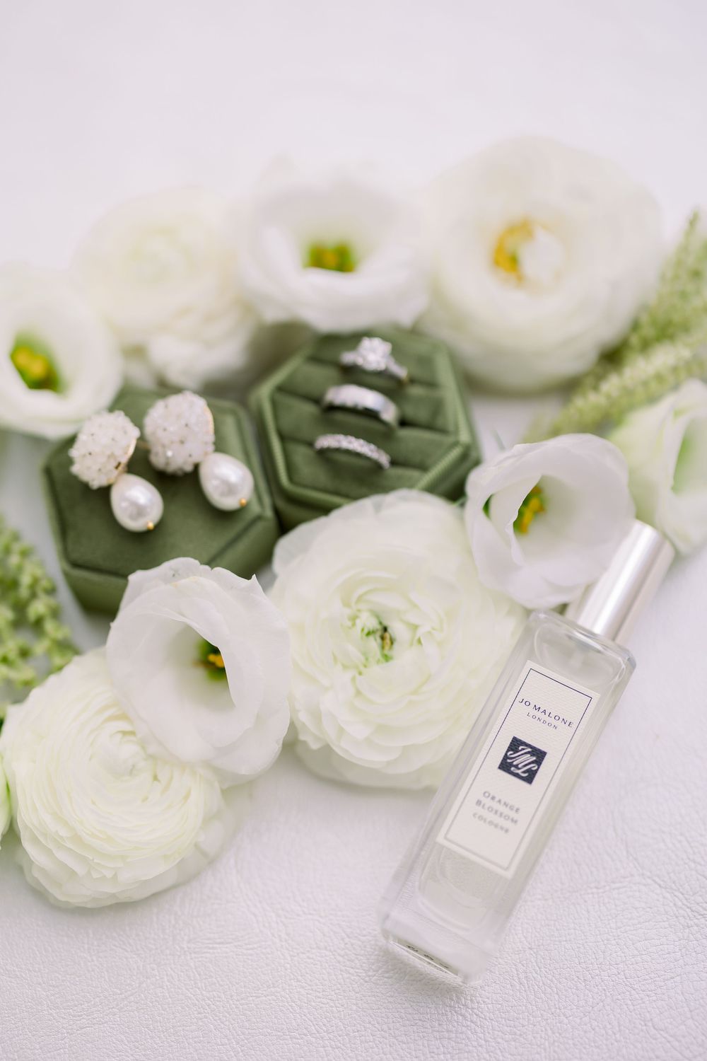 White ranunculus flowers and perfume bottles arranged with green accents on light background.