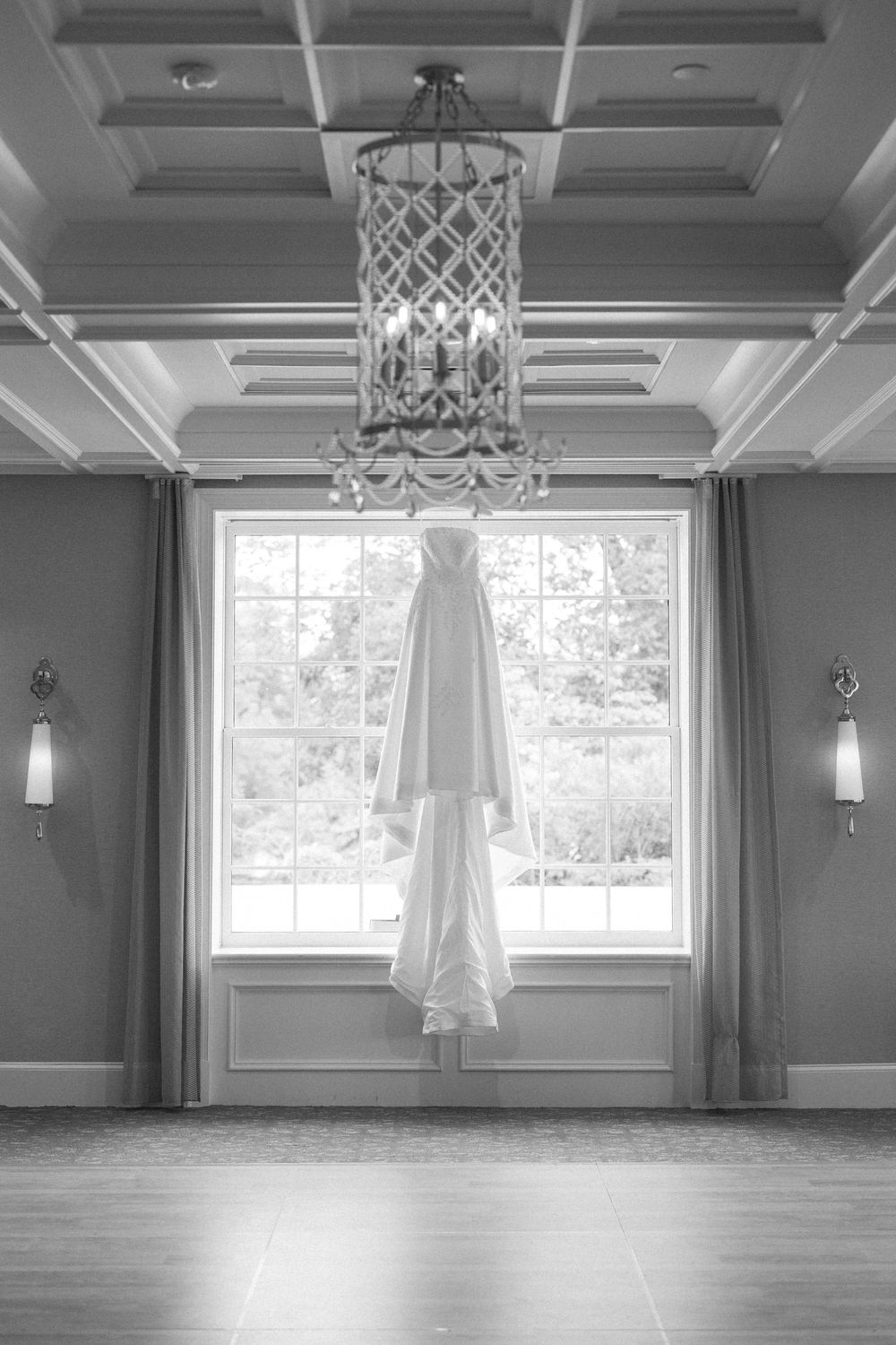 Empty wedding venue room with elegant chandeliers and natural light streaming through large windows.