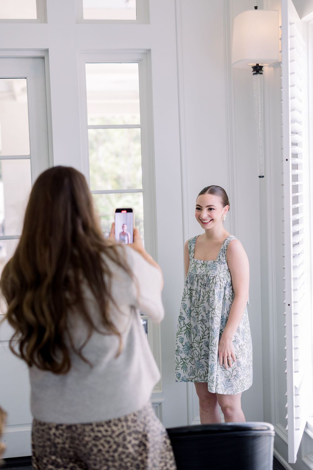 A behind-the-scenes photo shoot in a bright white room with natural lighting through tall windows.