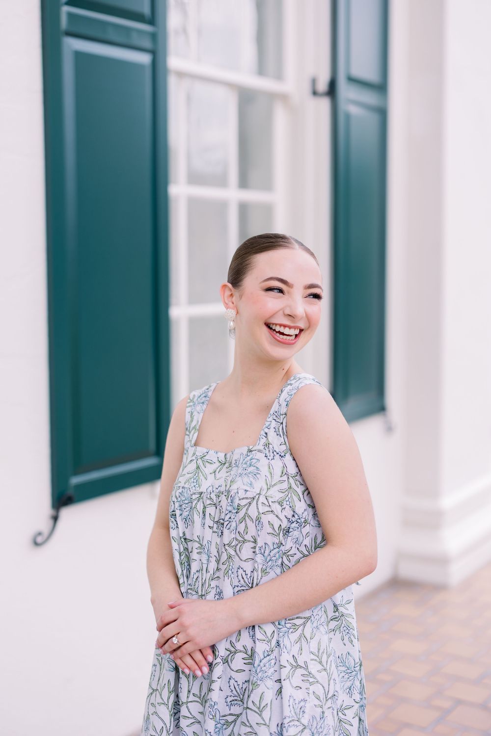A portrait session outdoors featuring a floral print sundress against a white building with green shutters.