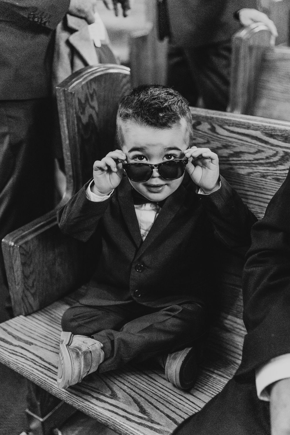 Young children in formal attire wearing sunglasses sit on a striped bench.