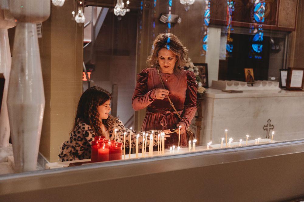 Two people light candles together in a festive indoor setting with blue decorative lights.