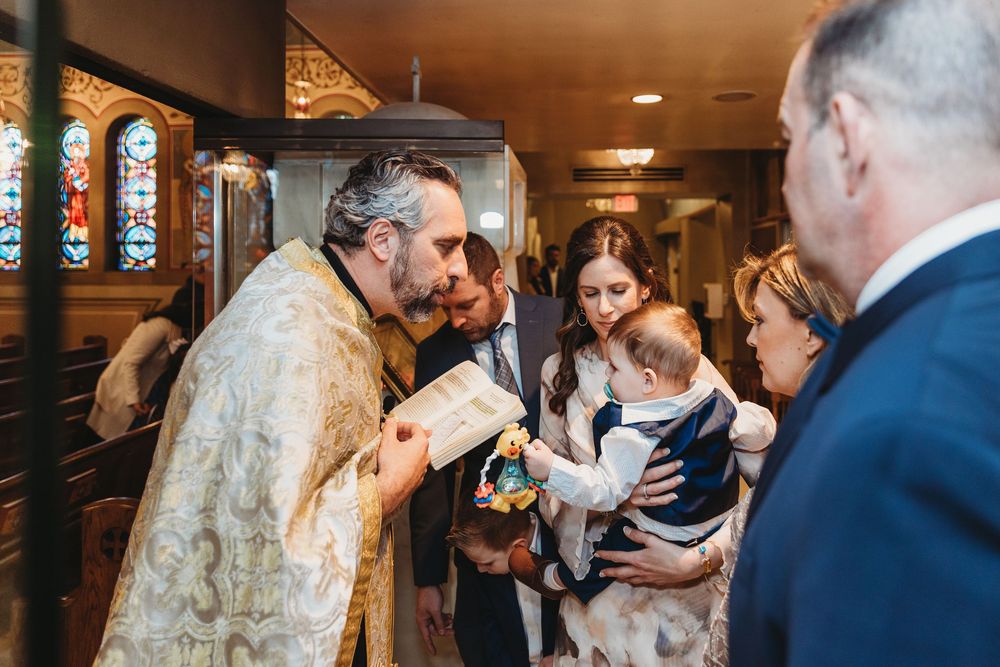 Orthodox priest in traditional vestments reads from a book during a religious ceremony with attendees.