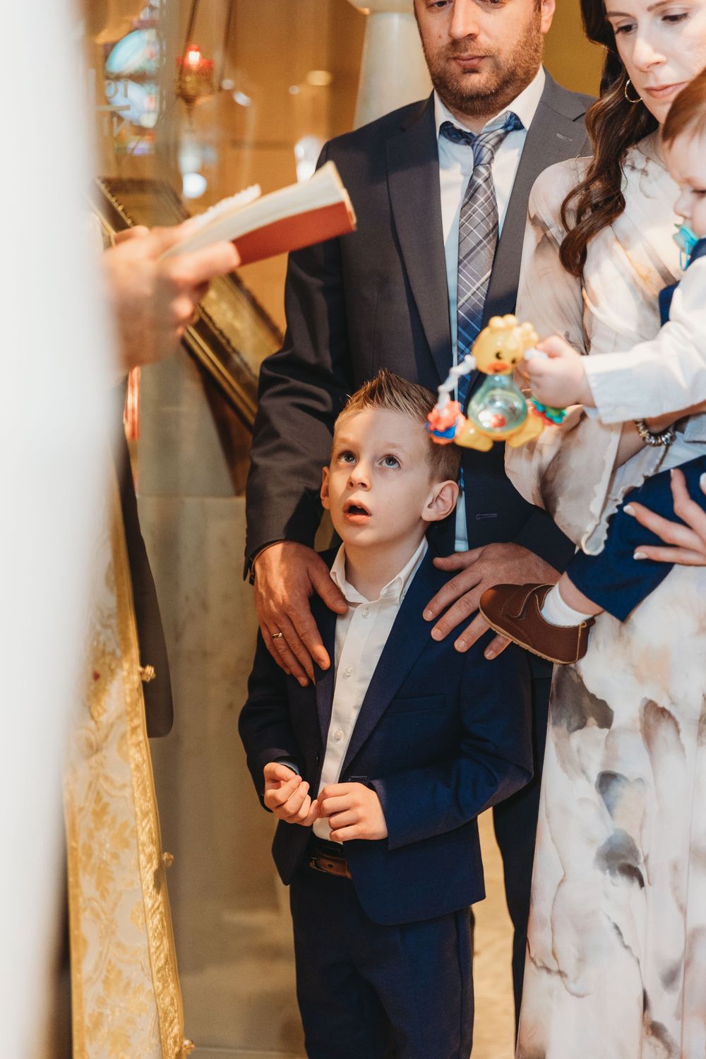A young child in a navy suit reacts with wonder as confetti falls during a wedding celebration.