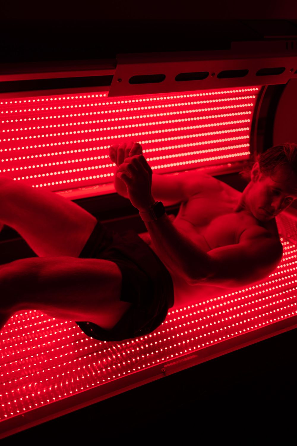 Person lying under bright red LED light therapy panels in a spa setting.