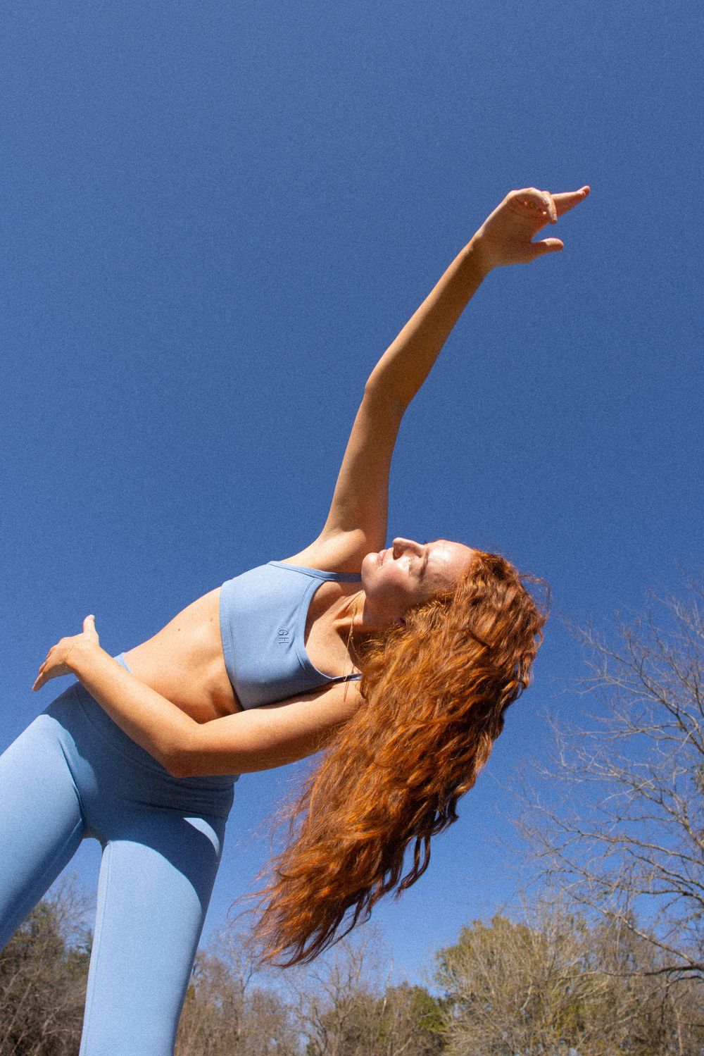 Person in blue athletic wear performing graceful backbend against bright sky background.