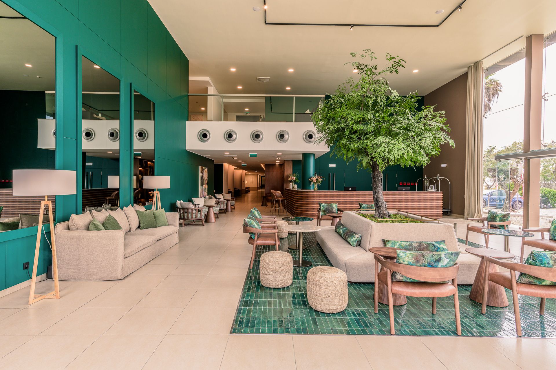 Modern coworking space interior with teal walls, wooden furniture, and abundant natural lighting throughout the open layout.