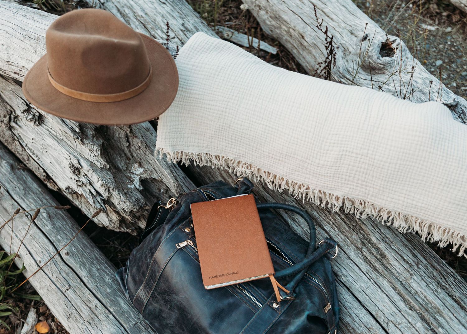Brown leather wallet and accessories arranged on weathered wooden surface with natural lighting.