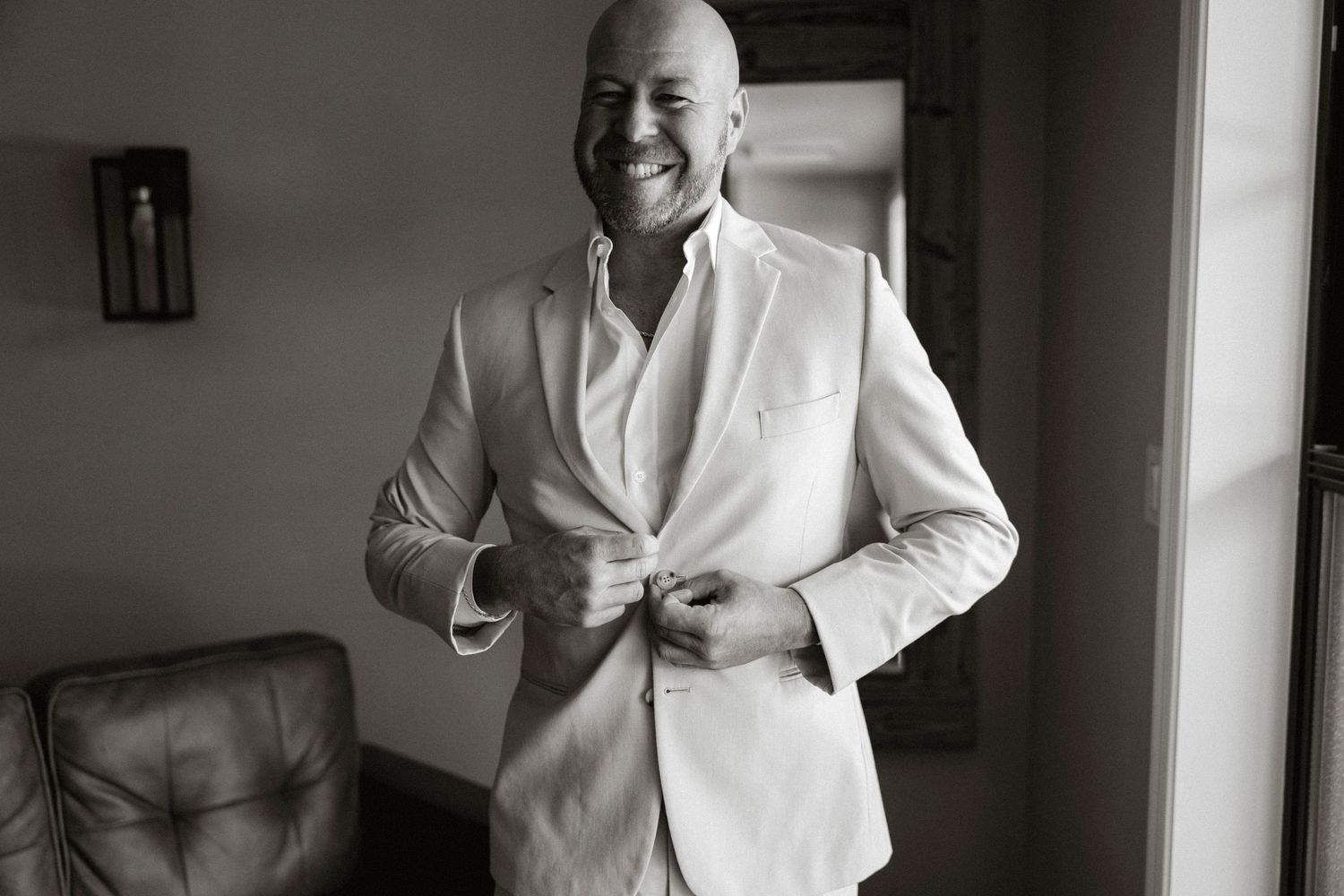 A person wearing a white shirt stands smiling in a well-lit room with modern decor.