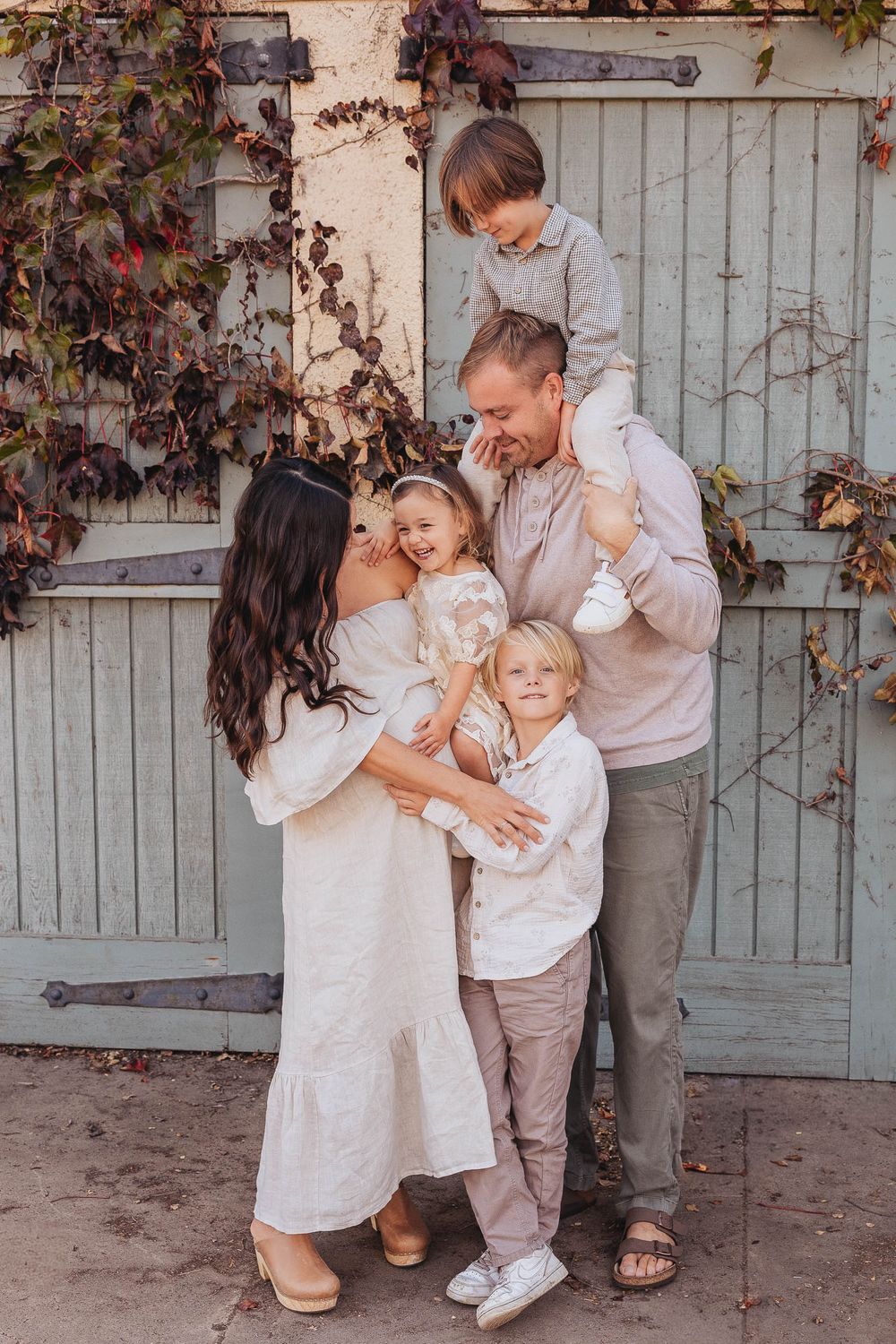 Candid family portrait in warm tones showing a tender moment together against a vintage door with autumn vines.