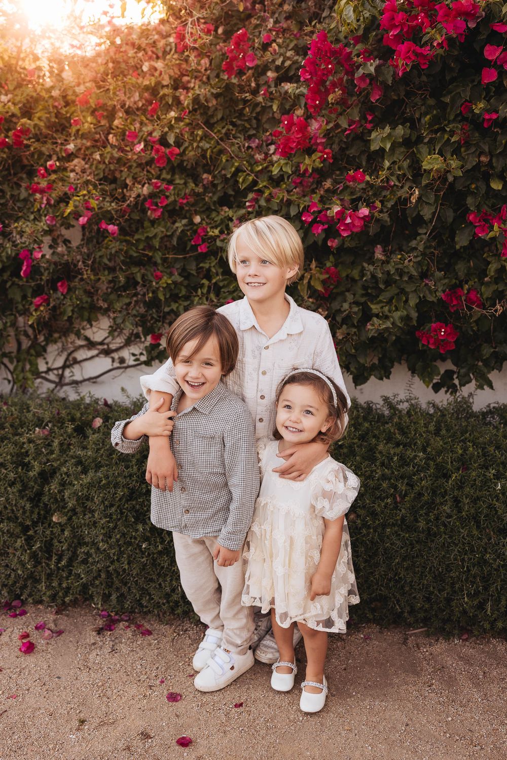 Children sit together in front of a vibrant wall of red bougainvillea flowers during golden hour.