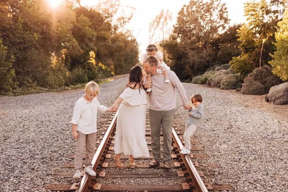 Family walks along train tracks at sunset creating a beautiful silhouette against the golden sky.