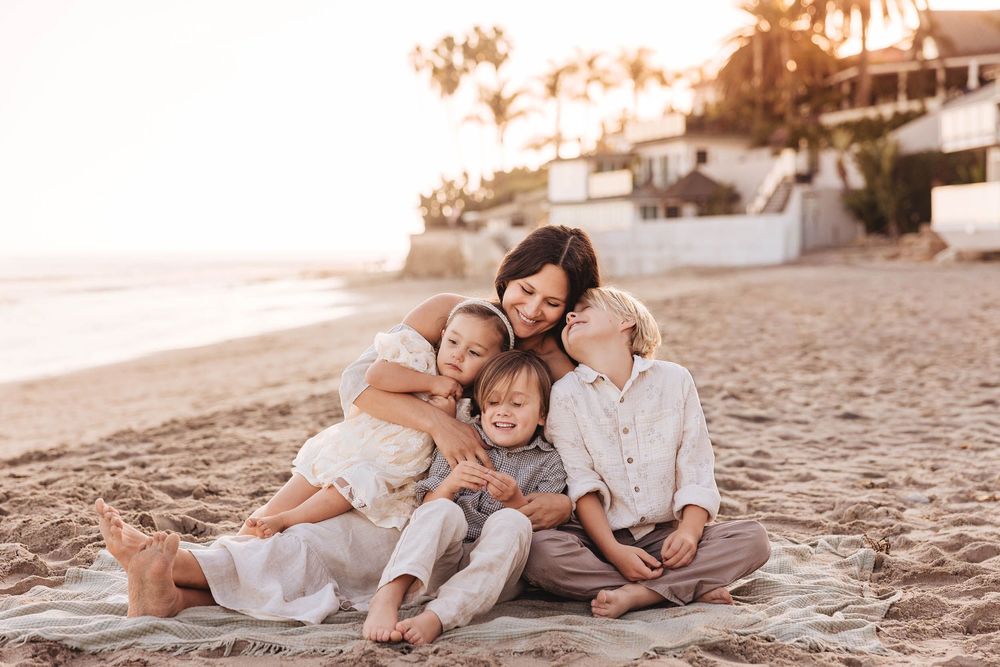 Family enjoys tender moments together on a sandy beach during sunset.
