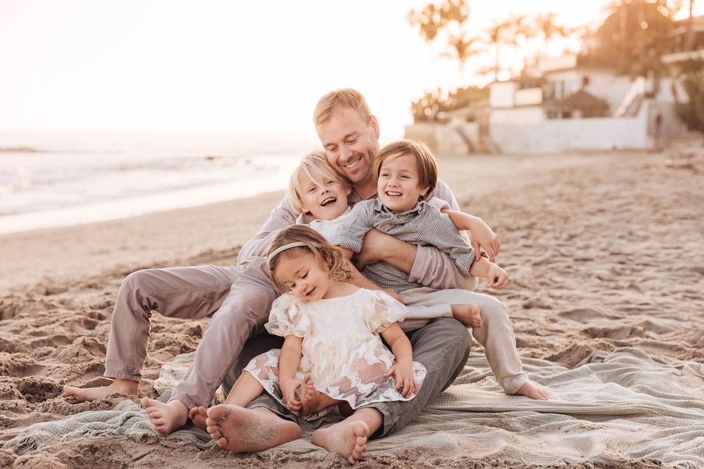A joyful moment shared on the beach sand with coastal houses and palm trees in the background.