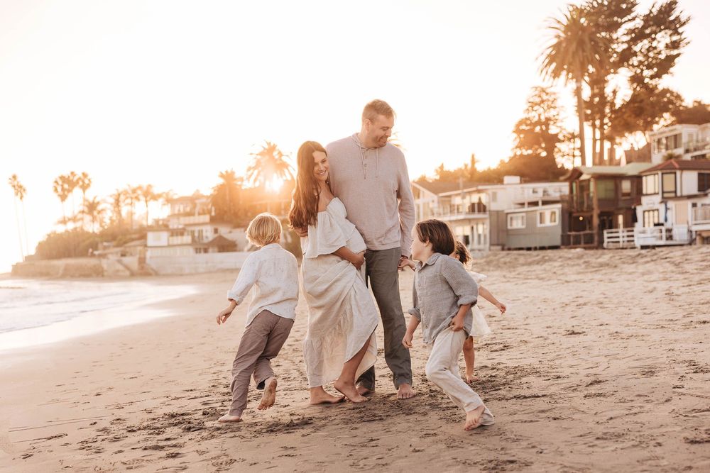 Family playing and laughing together on sandy beach at golden hour.