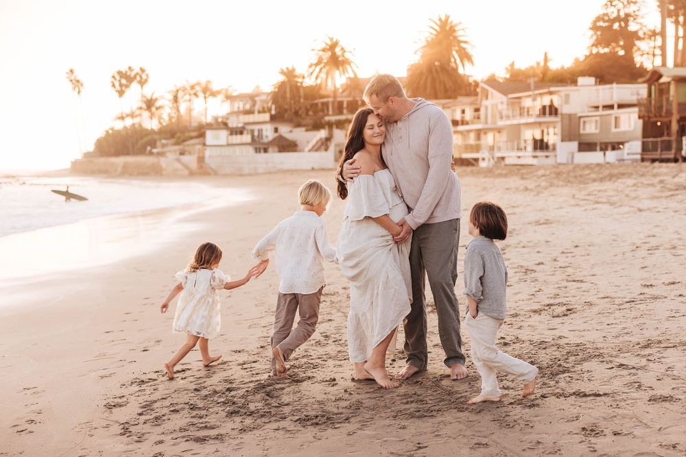 Family enjoying a sunset walk together on a beach with coastal homes and palm trees in the background.