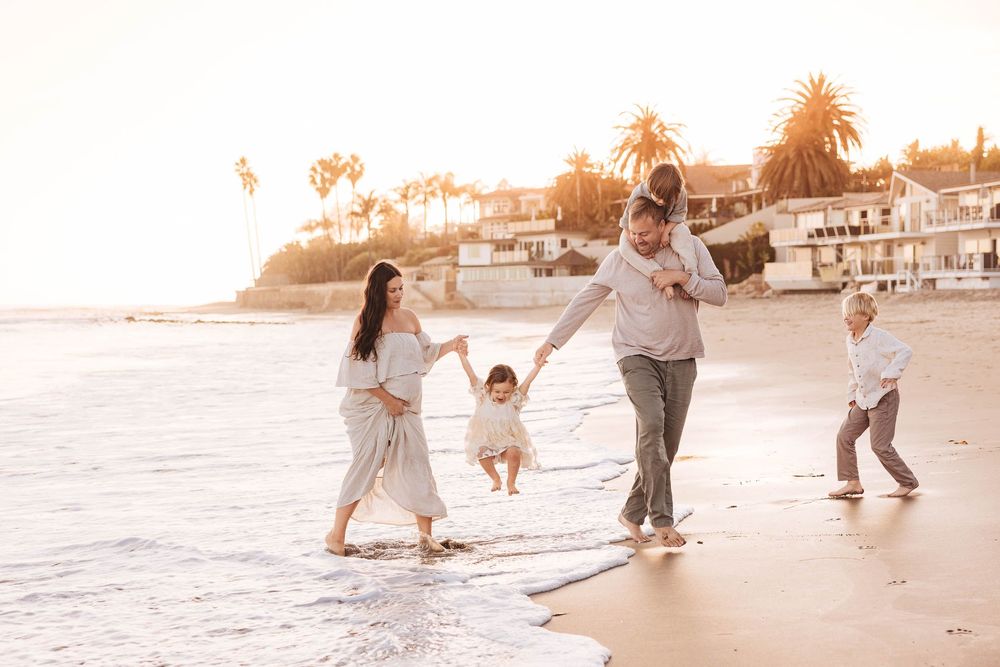 Family playing and jumping together at the beach during golden hour with coastal scenery.