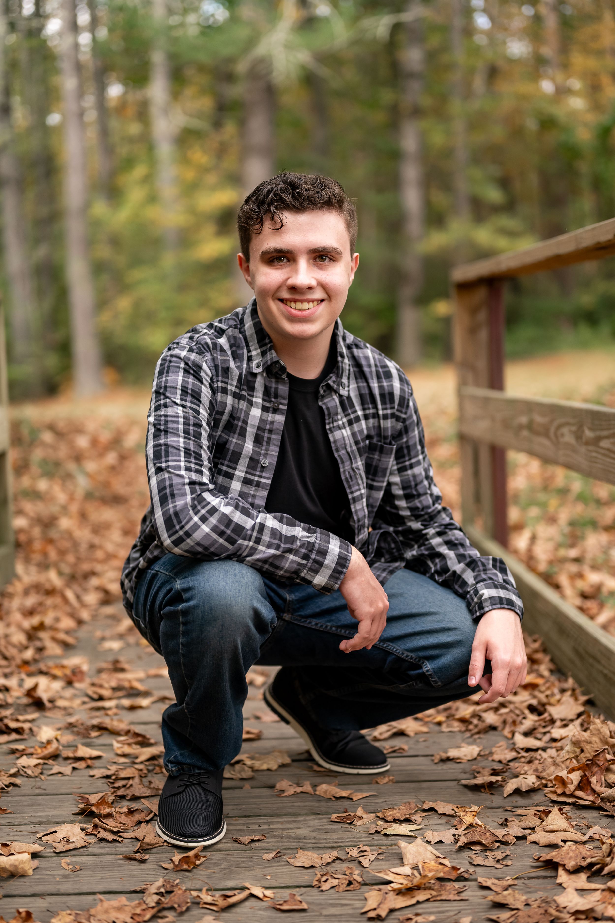 Casual outdoor portrait series on wooden boardwalk surrounded by fallen autumn leaves in wooded setting.