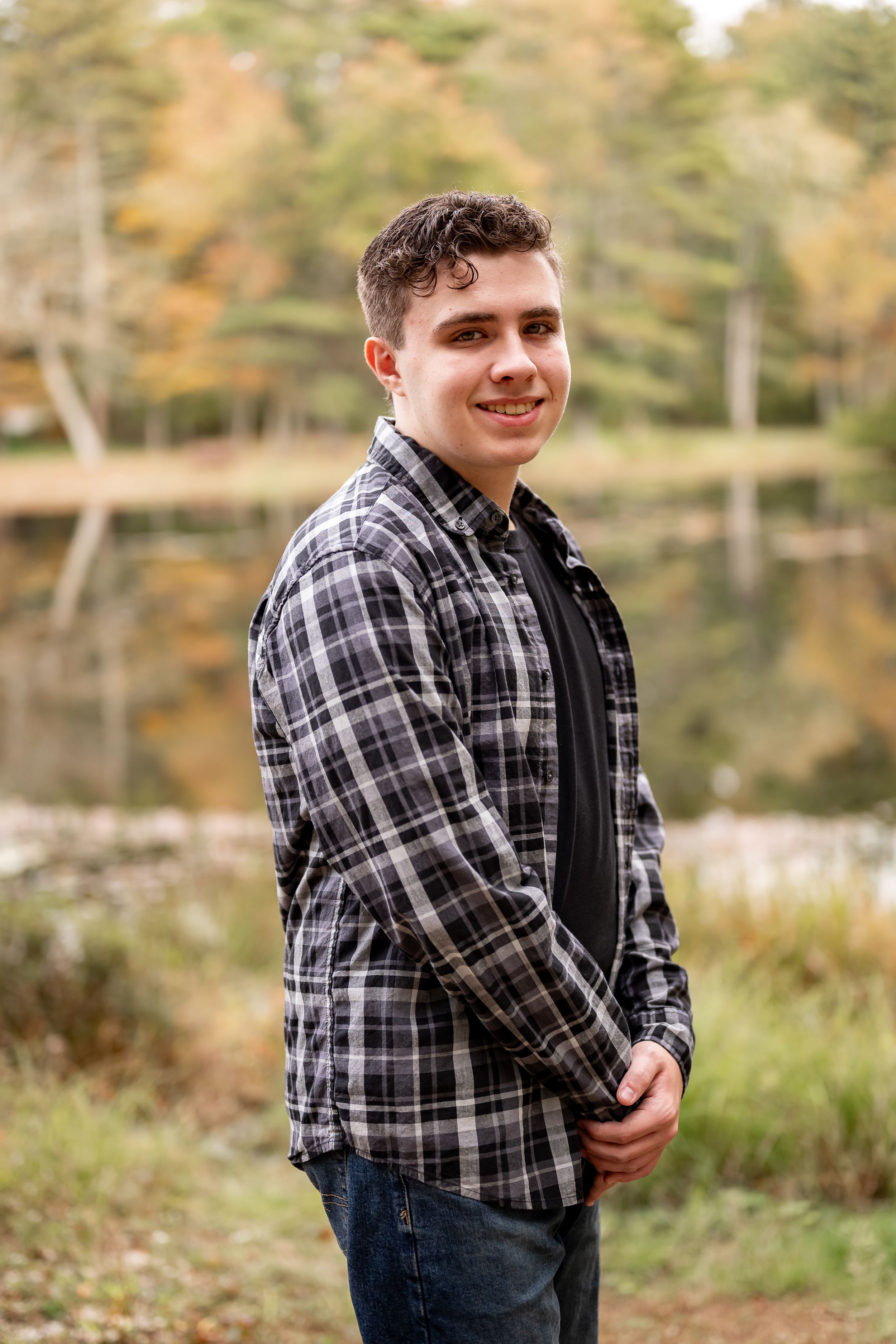 Outdoor portrait series showing casual style with plaid flannel shirt against natural fall foliage background.