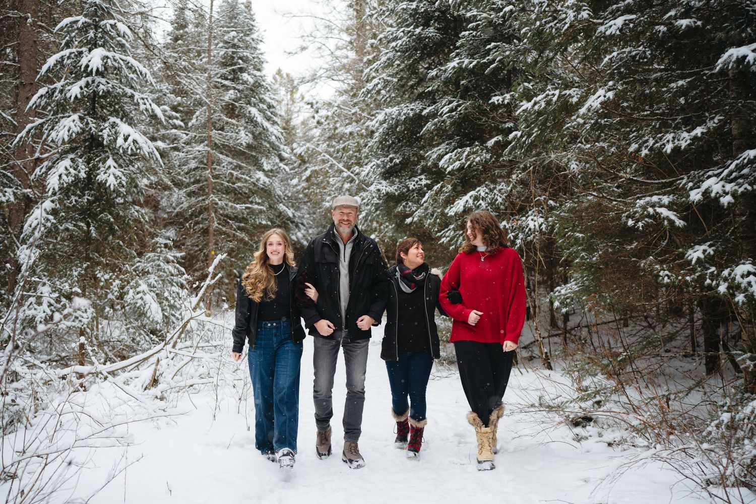 A group of people walking together on a snow-covered path through evergreen trees in winter.