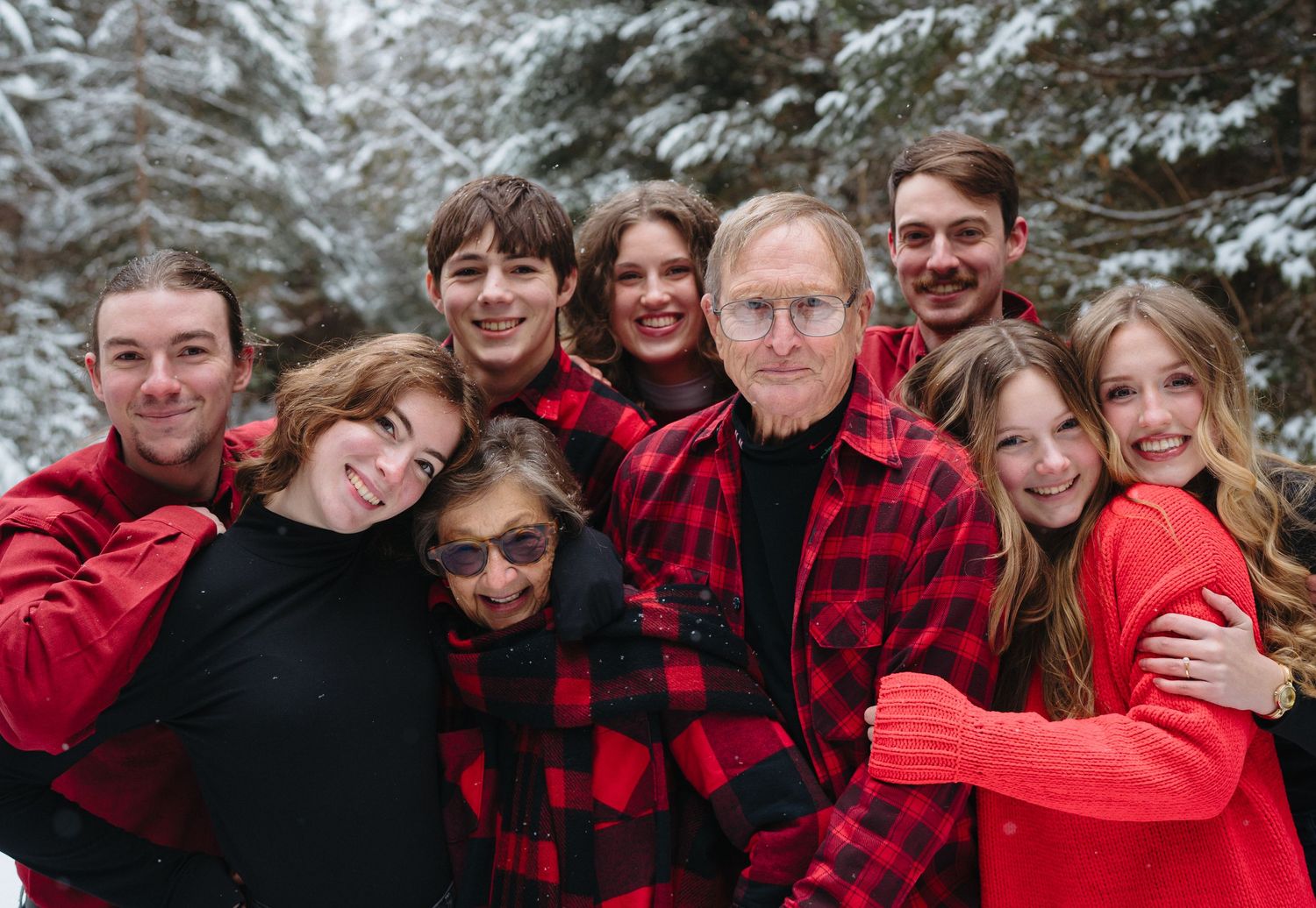 Extended family wearing coordinated red and black outfits poses together in snowy winter setting.