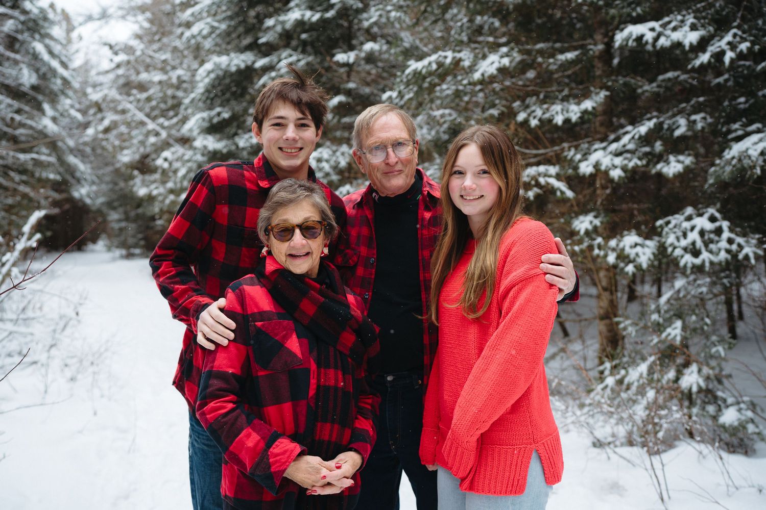 Group of people posing together in winter attire against a snowy forest backdrop wearing red and plaid.