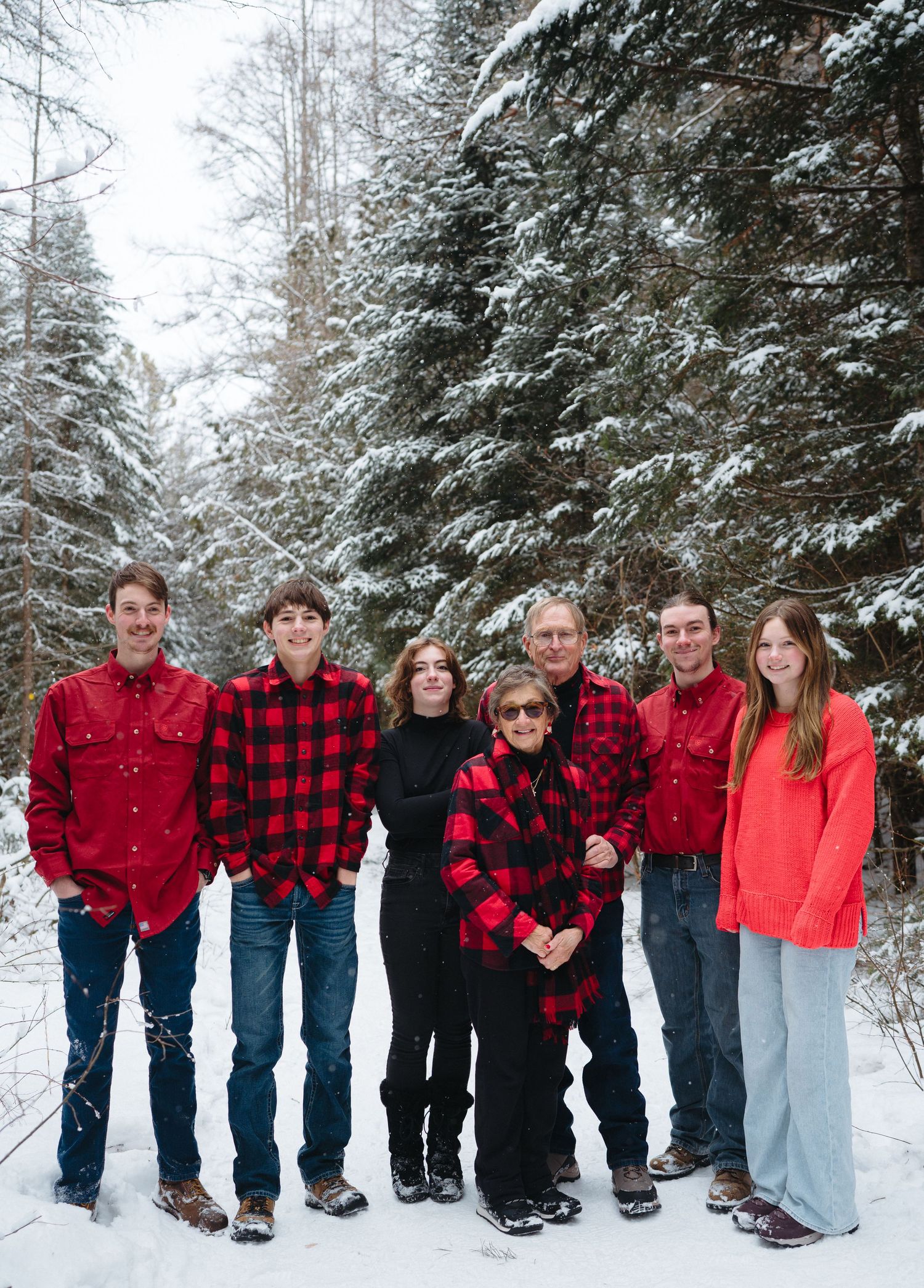 Group photo in a snowy forest with people wearing coordinated red and plaid outfits standing in a line.