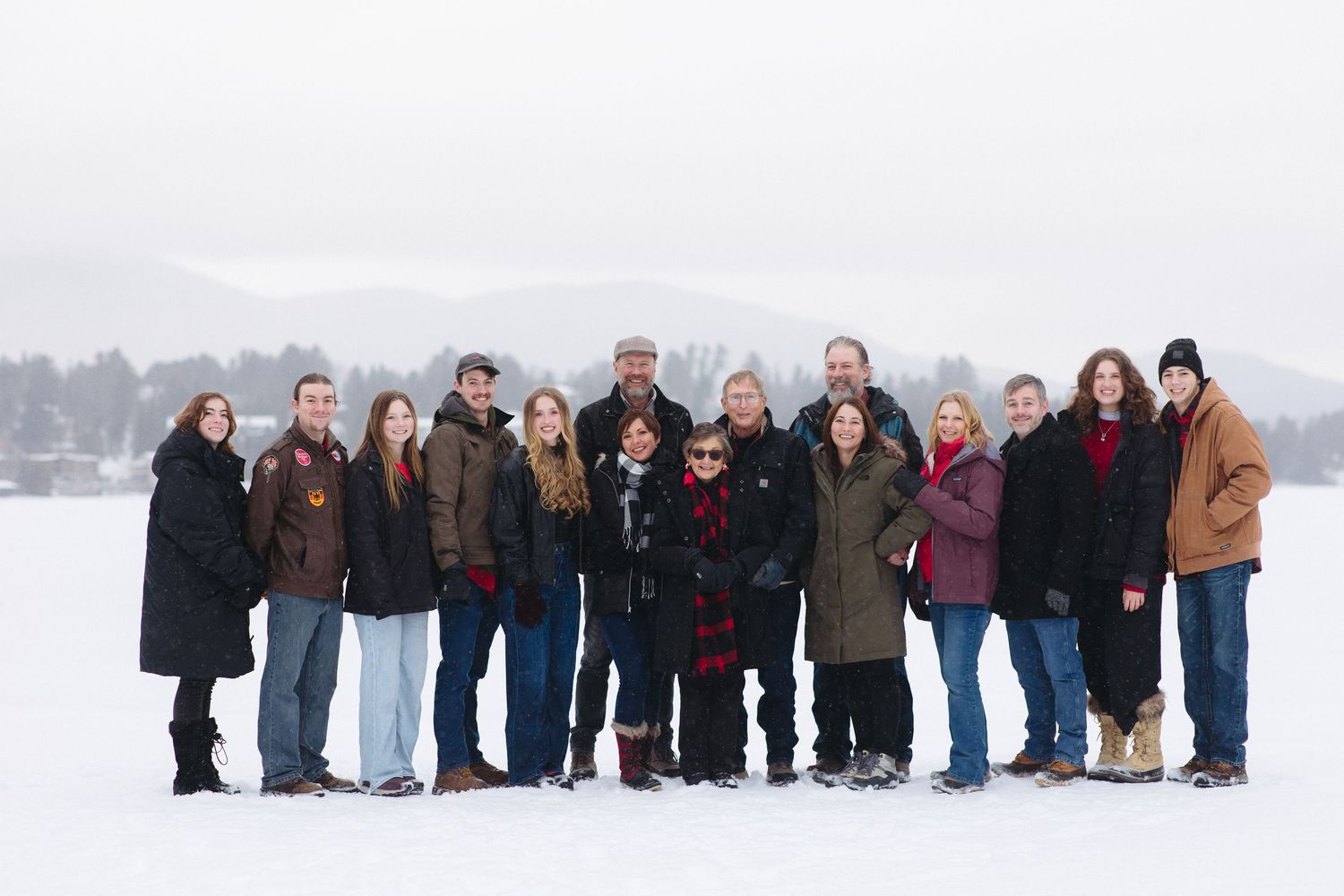 Large group photo of family members lined up in snow with evergreen trees in background.