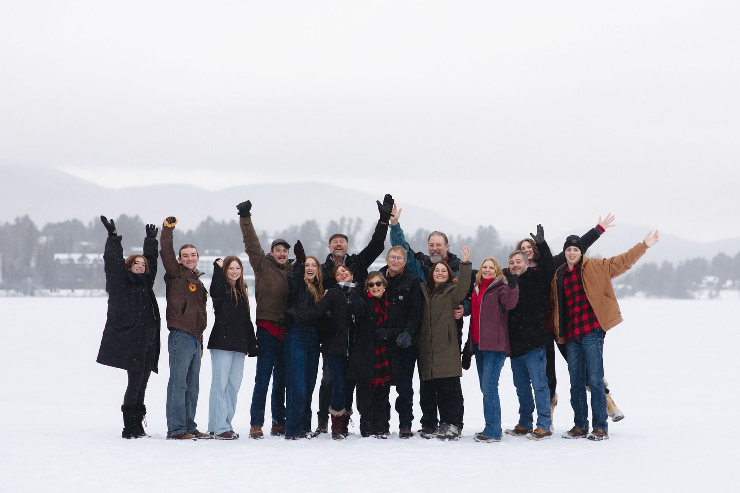 People stand in a line on a snowy field with arms raised against a winter landscape.