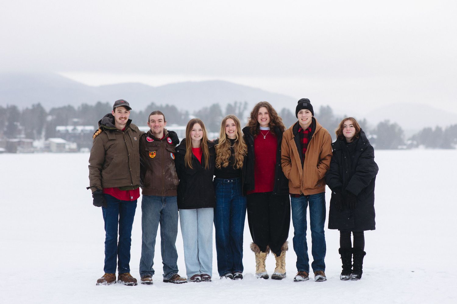 A group of people stand together in a line against a snowy winter landscape backdrop.