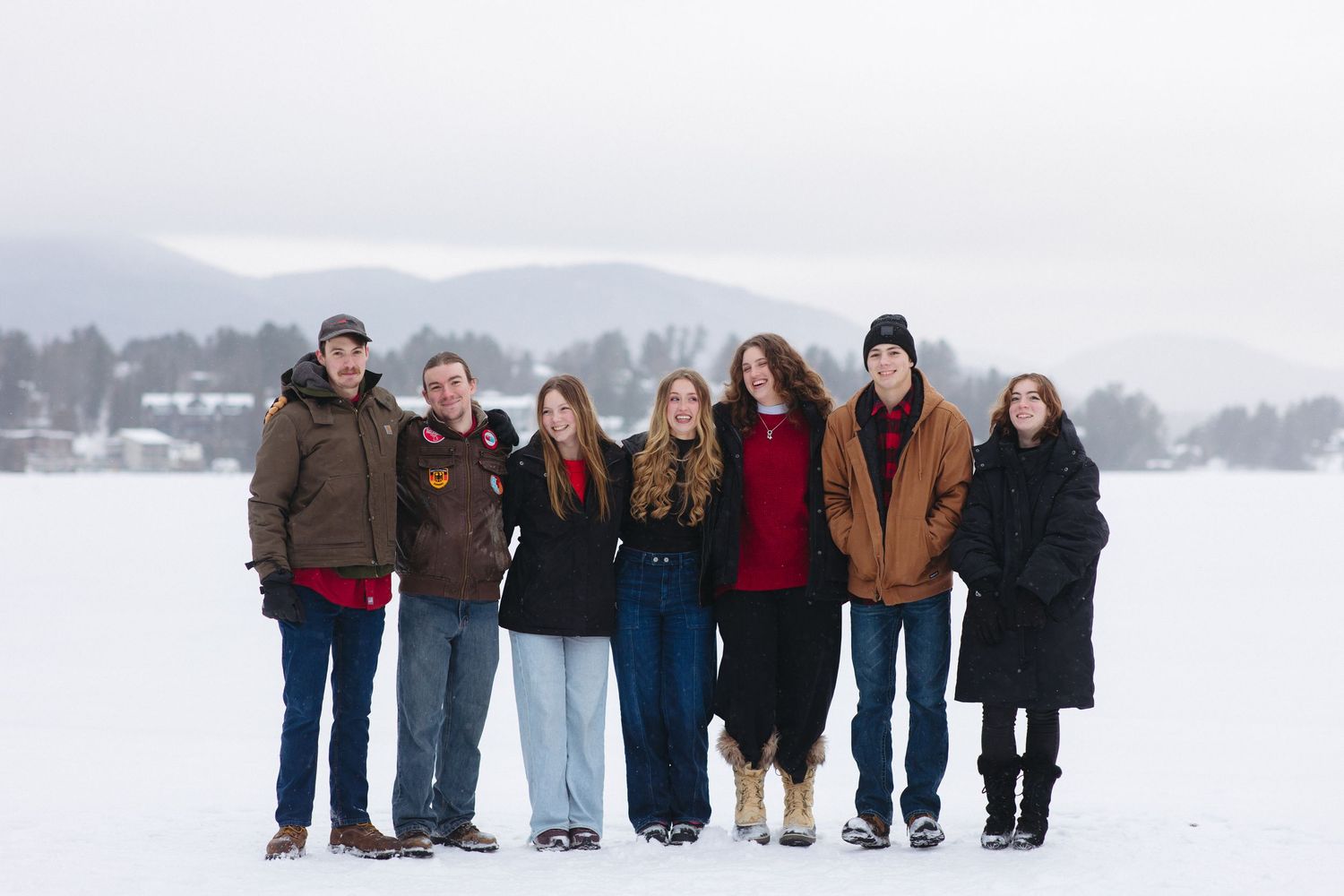 Large group of people lined up for a photo on a frozen snow-covered lake with winter landscape behind them.
