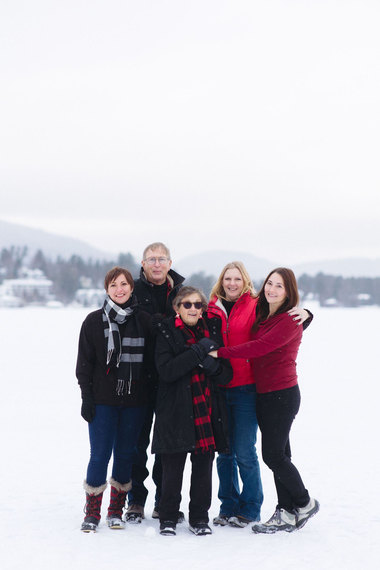 A group poses playfully in the snow with winter attire against a white landscape backdrop.