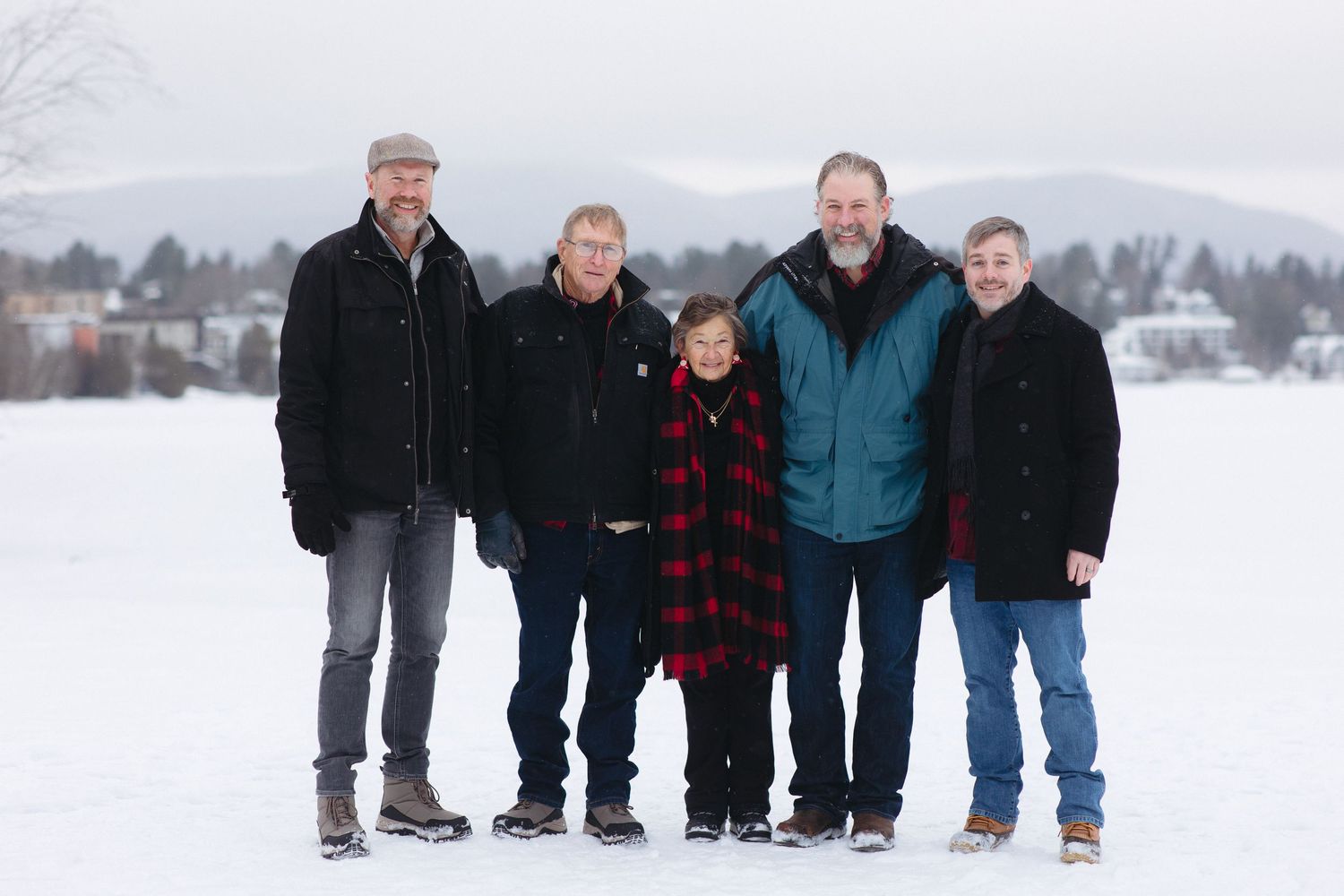 A group of people standing together in winter clothing on a snowy landscape with mountains in the background.