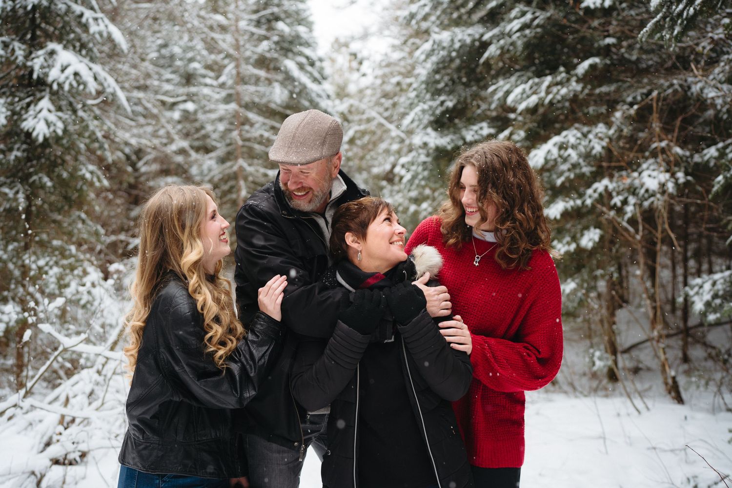 A family of four shares a candid moment together on a snow-covered forest path in winter.