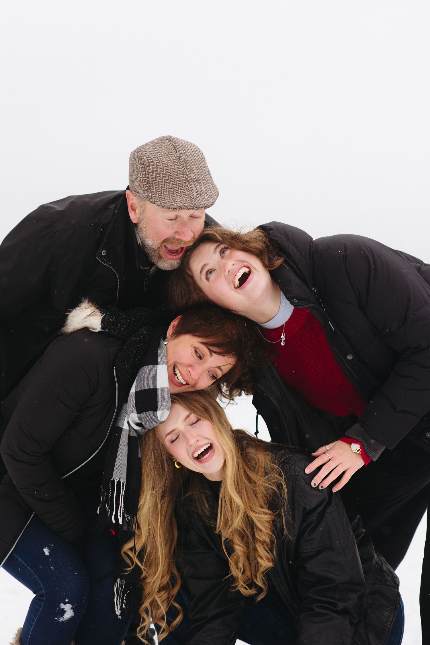 A joyful group in winter coats and hats share a candid laughing moment together against a white background.