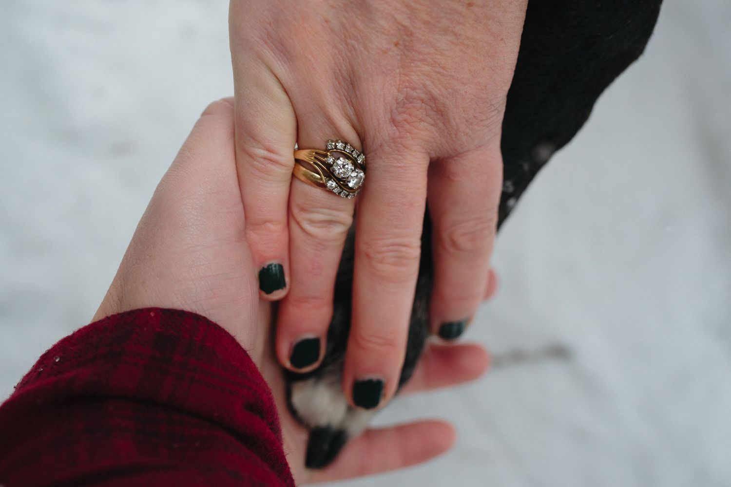Close-up view of hands with black nail polish holding a small silver ring against a light background.