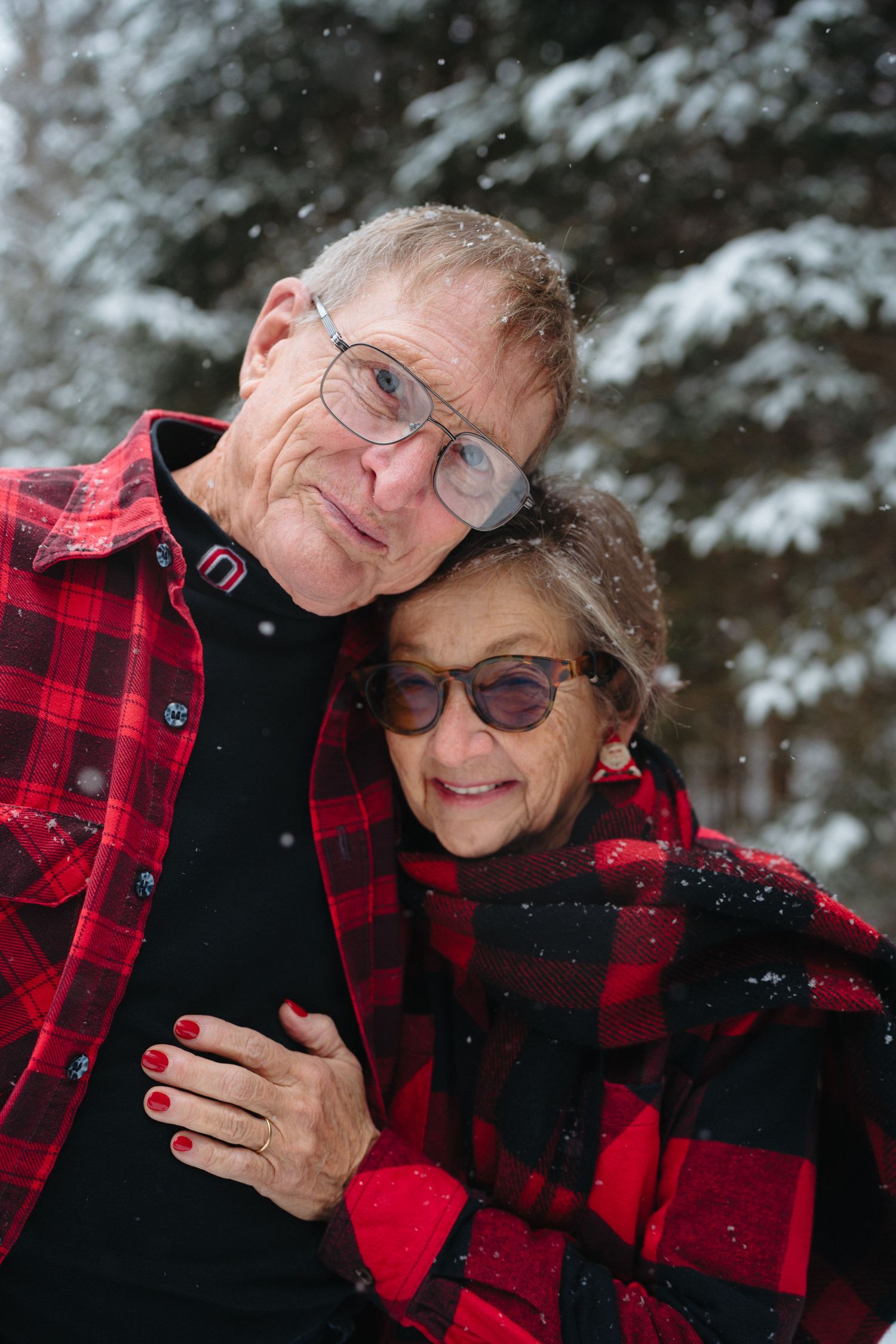 A couple wearing matching buffalo plaid jackets embrace in a snowy winter setting.
