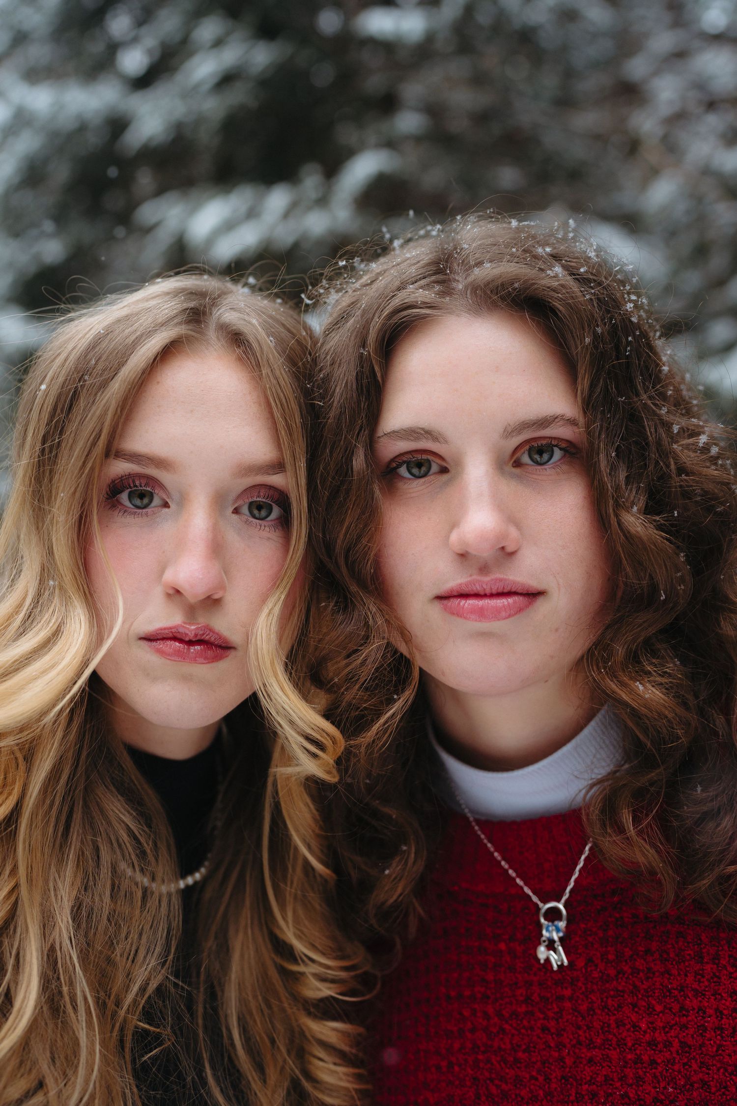 Close-up portraits in a winter setting showing two people in red sweaters with windswept hair.