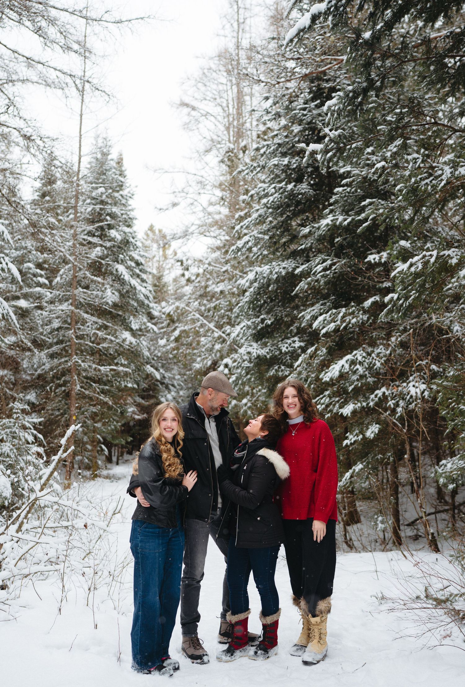 Family enjoying a winter day together in a snowy forest setting, laughing and having fun in matching winter attire.