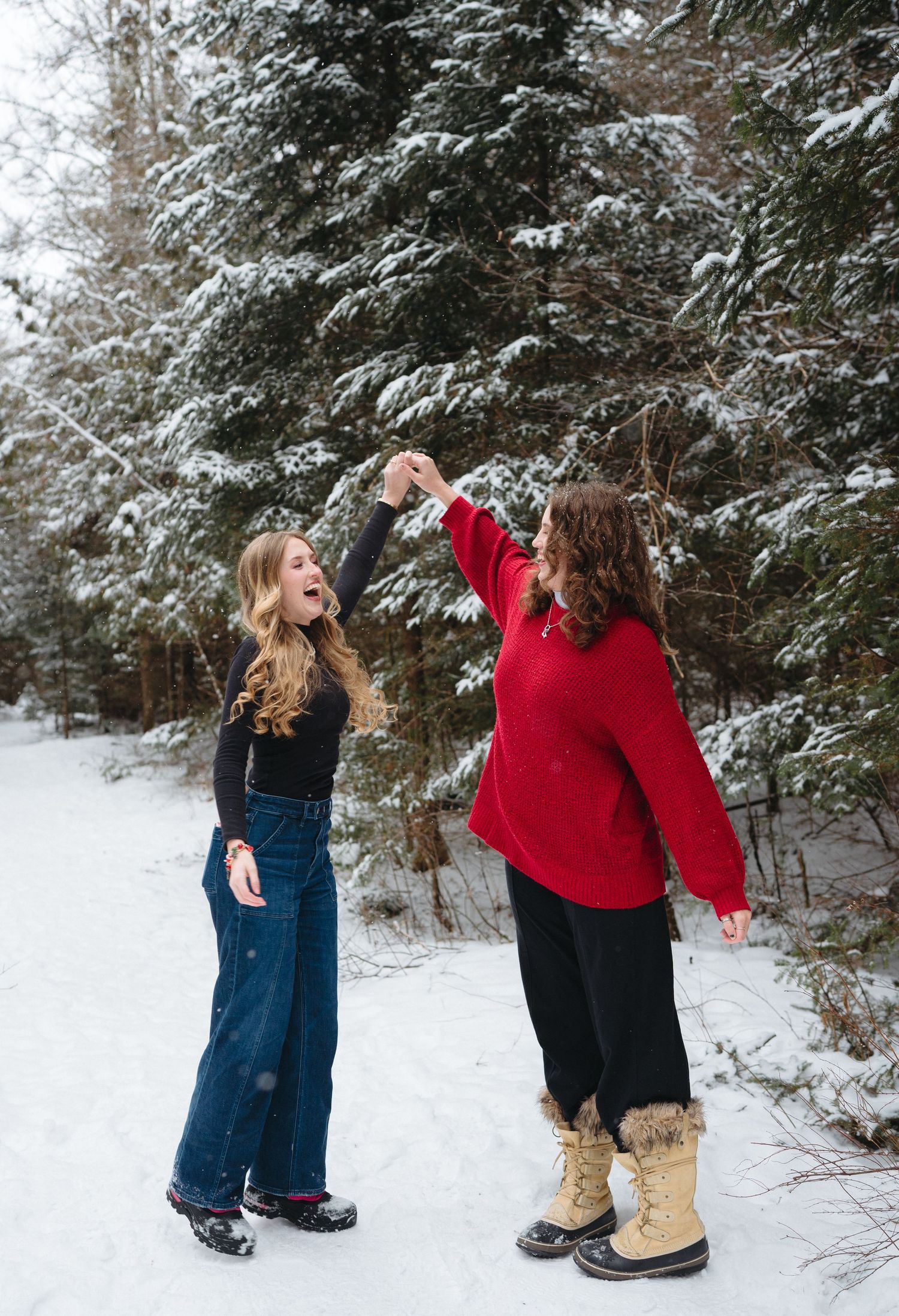 Two friends playfully throwing snow at each other in a winter forest setting with snow-covered evergreen trees.