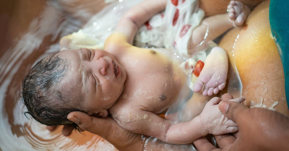 Close up of baby supported in birthing pool during water birth