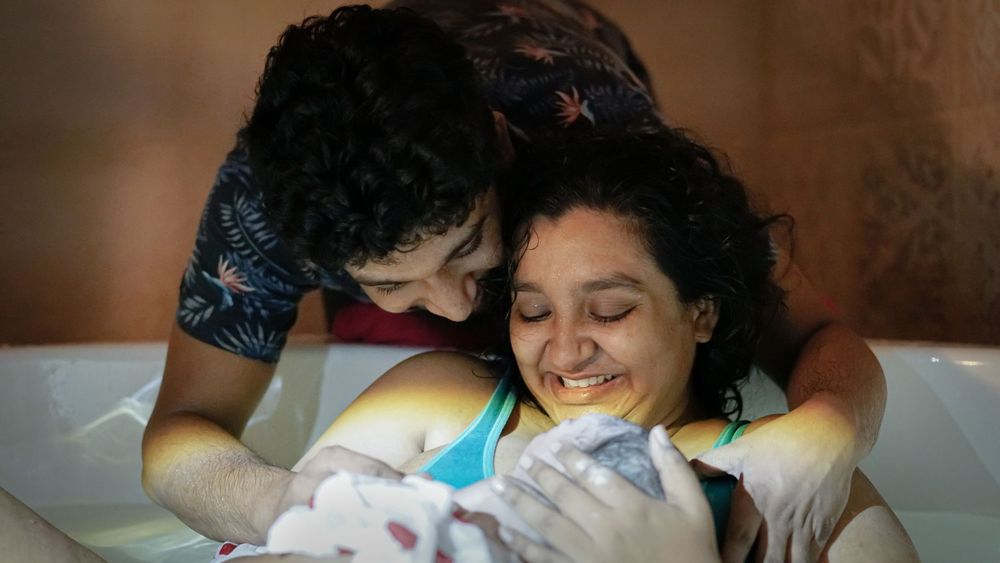 Parents embracing their baby immediately after a water birth in the birthing pool